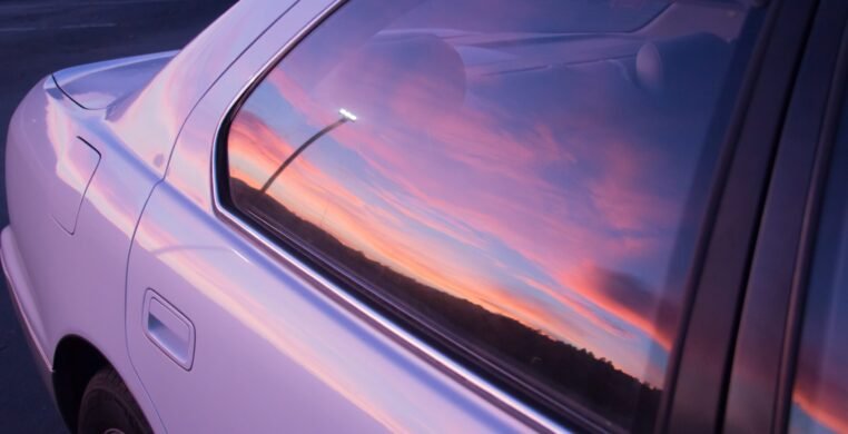 The beautiful colors of the sunset sky reflected in the window of a purple car